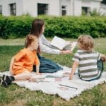 Kobieta uczy dwoje dzieci na kocu w parku, zabawa i nauka liczenia