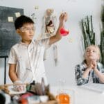 Dwoje dzieci robi doświadczenia chemiczne przy stole, uczy się i obserwuje
