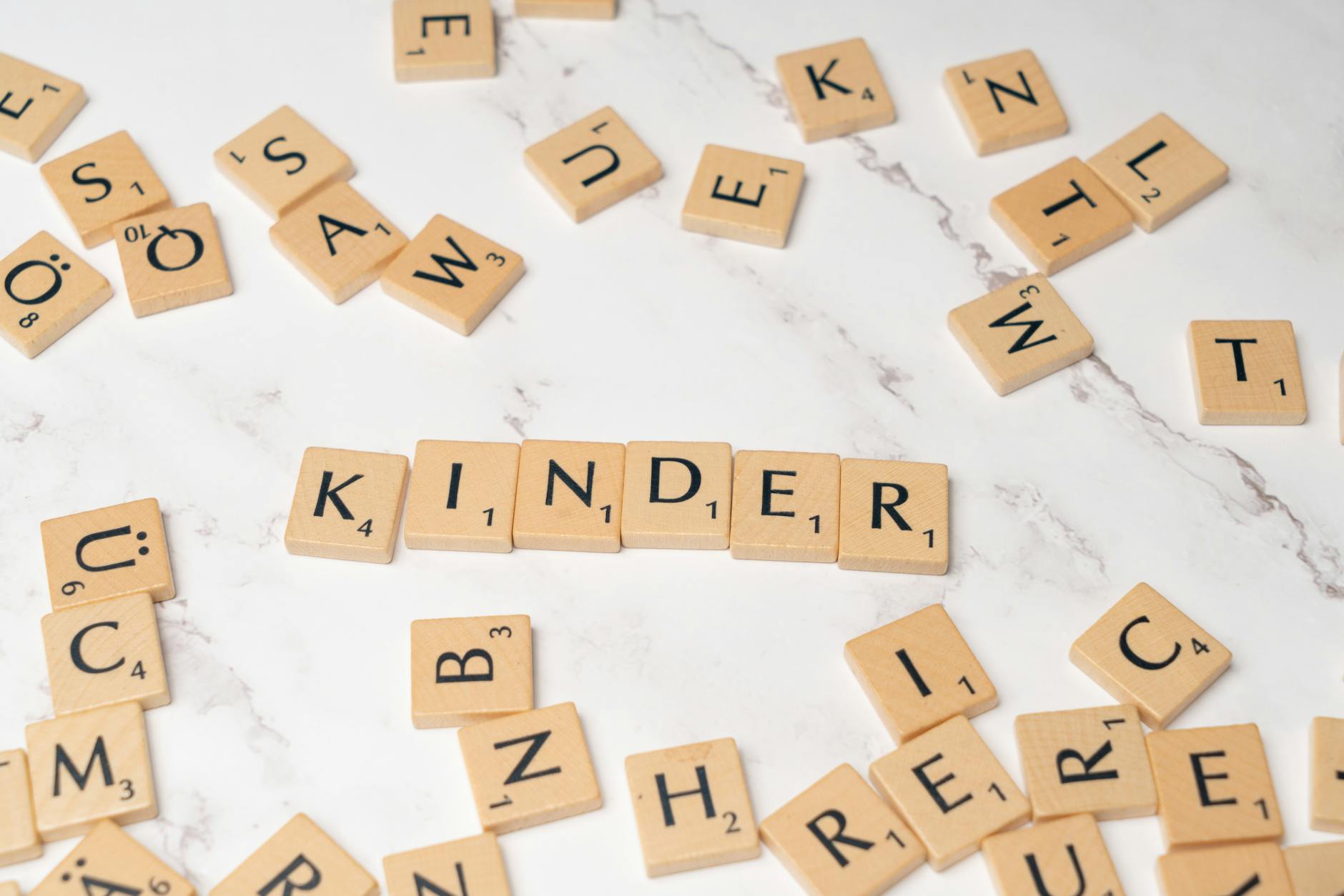 Drewniane litery scrabble układające się w słowo Kinder na marmurze