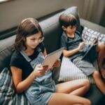 Dwoje dzieci na kanapie w domu pochłoniętych ekranami tabletów