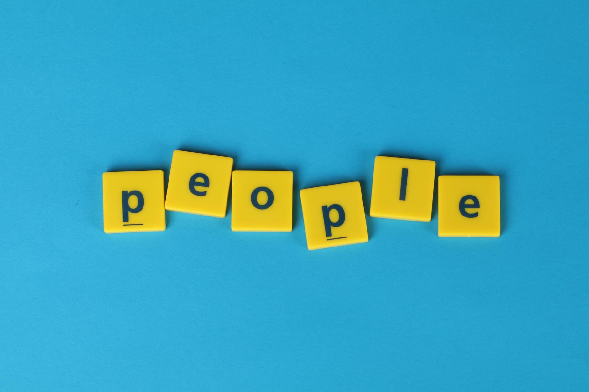 Żółte płytki Scrabble tworzące słowo people na niebieskim tle