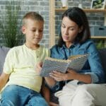Mama czytająca książkę synkowi na kanapie w przytulnym salonie