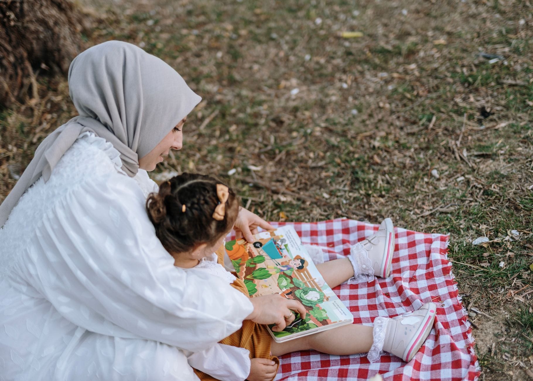 Mama w chuście czyta książkę z córką na kocu w parku